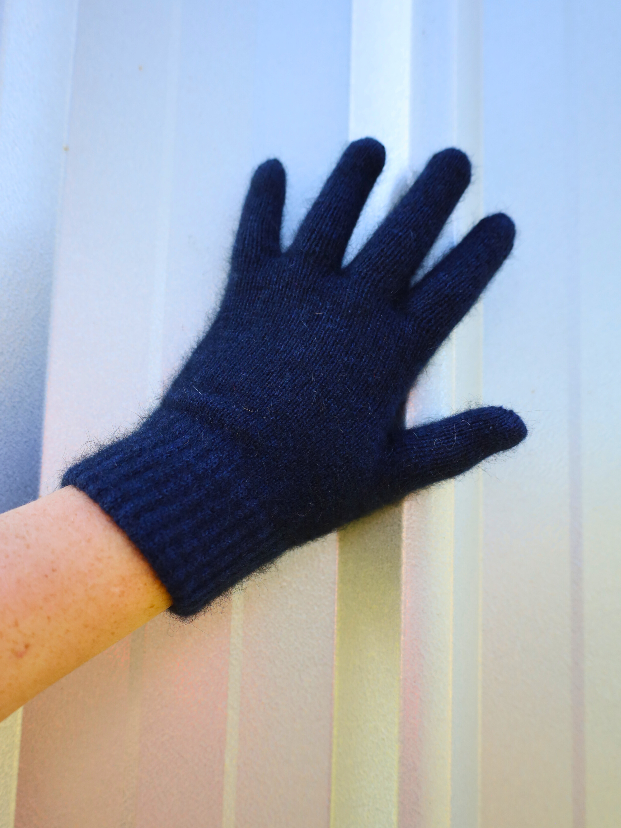 Navy blue glove on a person's hand against a light curtain background
