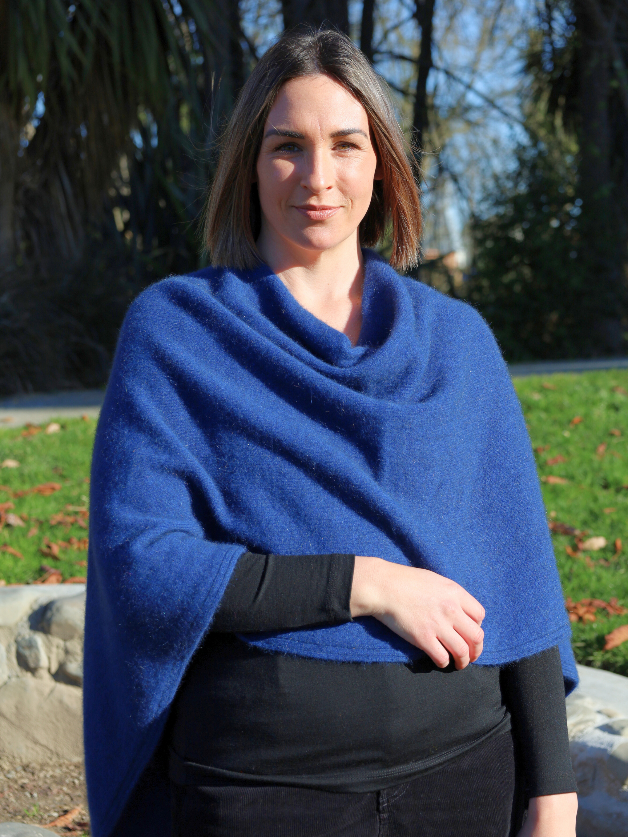 Woman wearing a blue poncho standing outdoors with trees and grass in the background