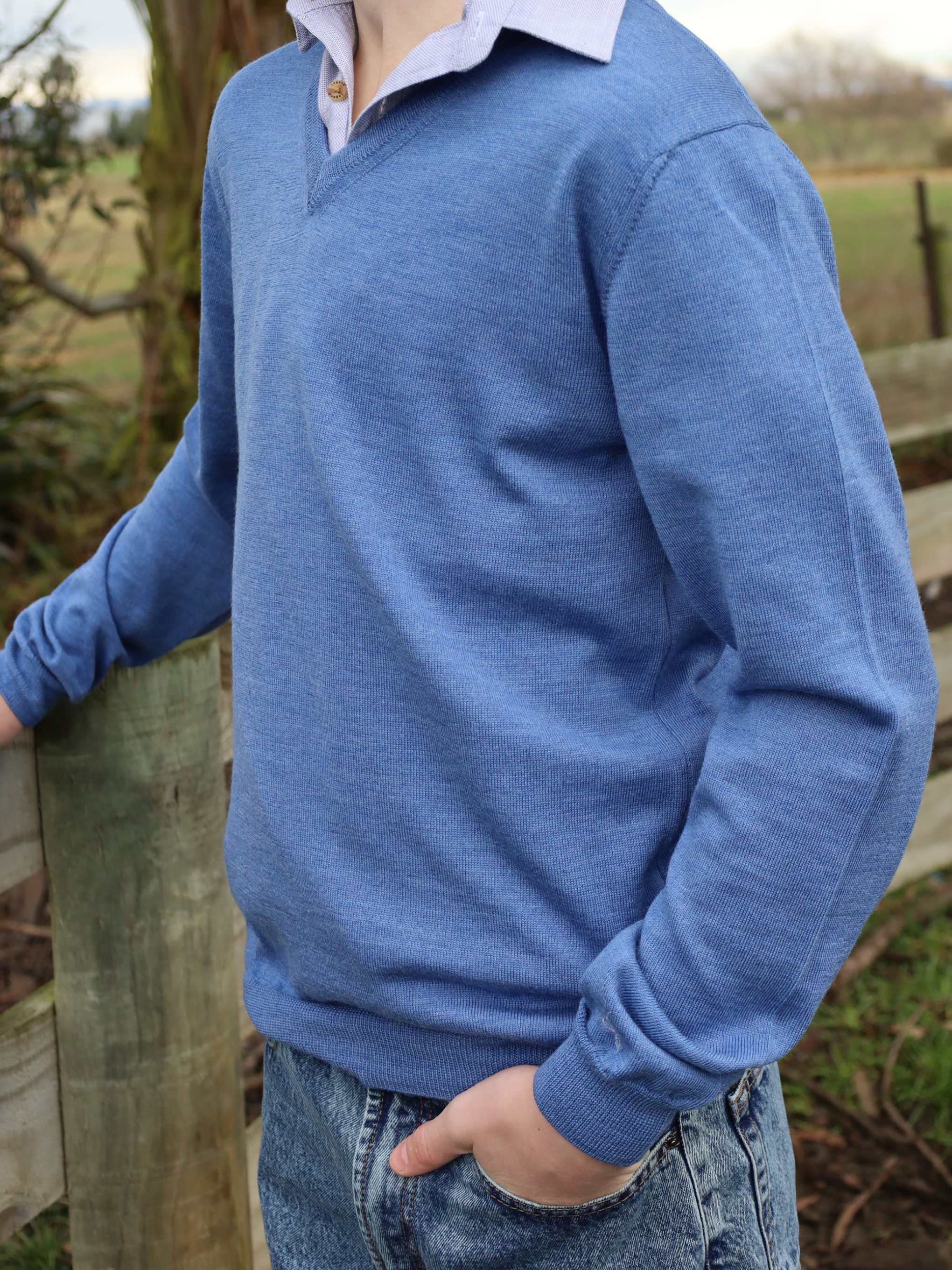 Person wearing a blue sweater standing outdoors near a wooden fence.
