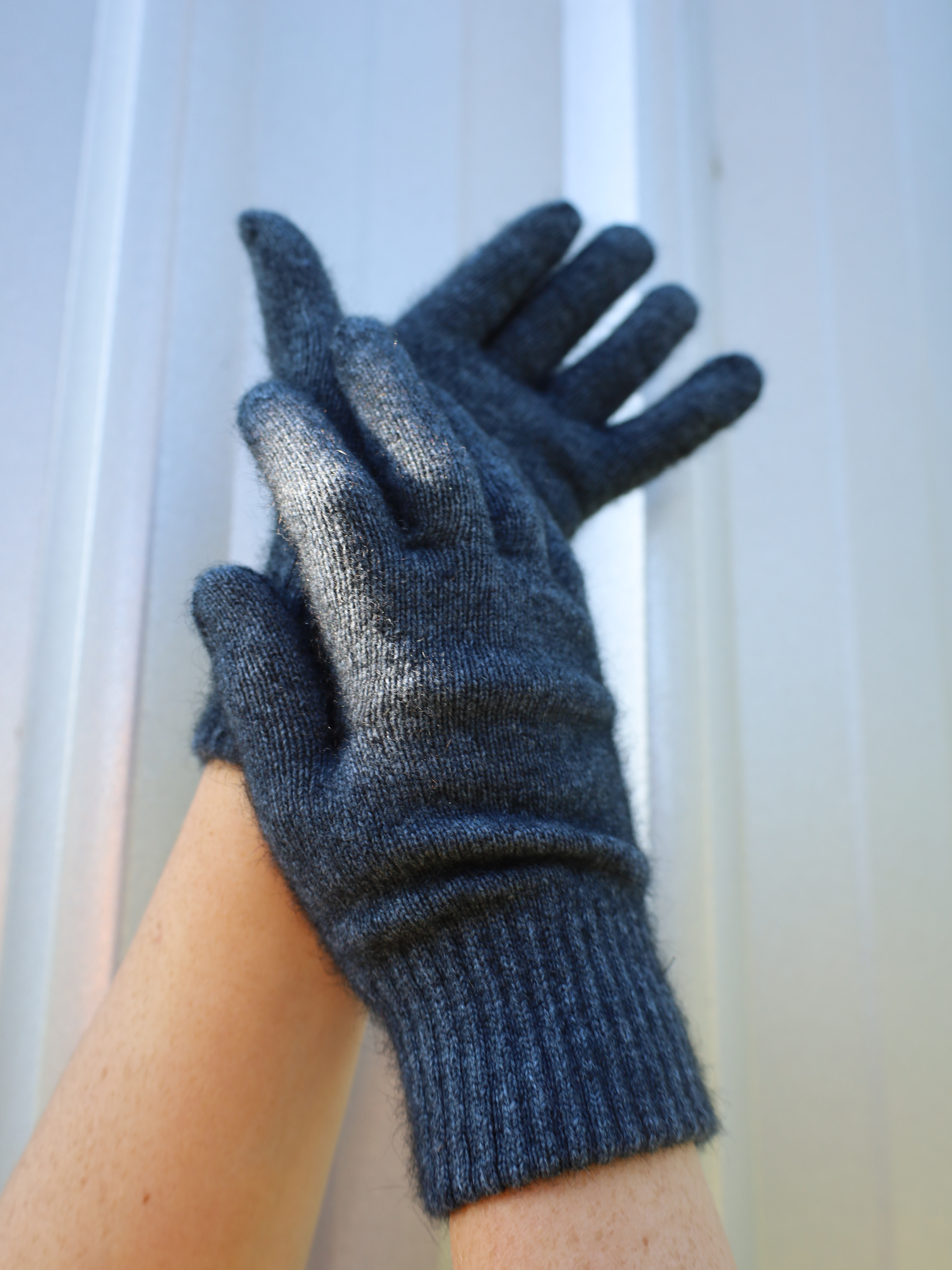 Pair of gray gloves held against a white wall