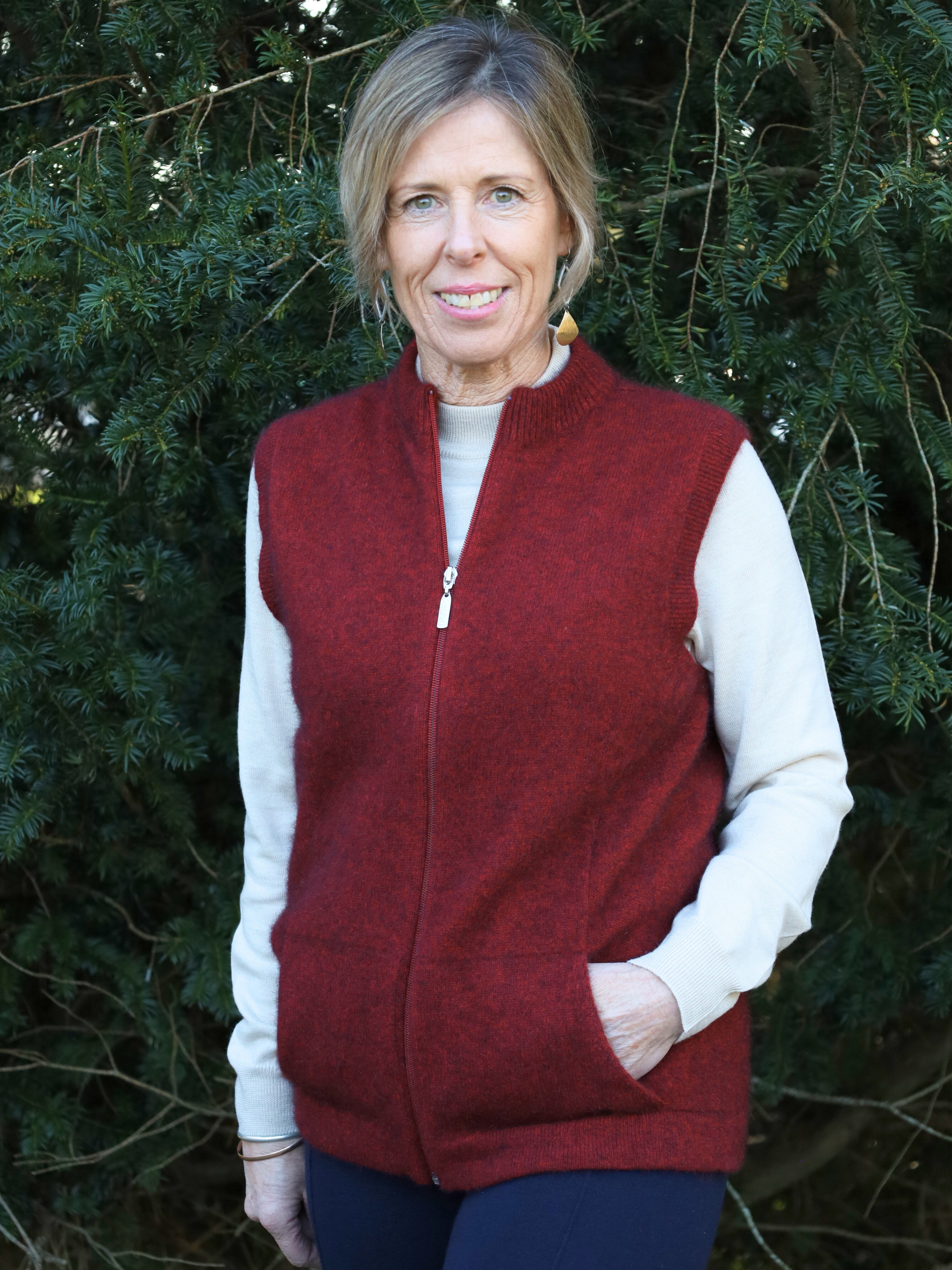 Woman wearing a red vest over a white shirt with a green leafy background