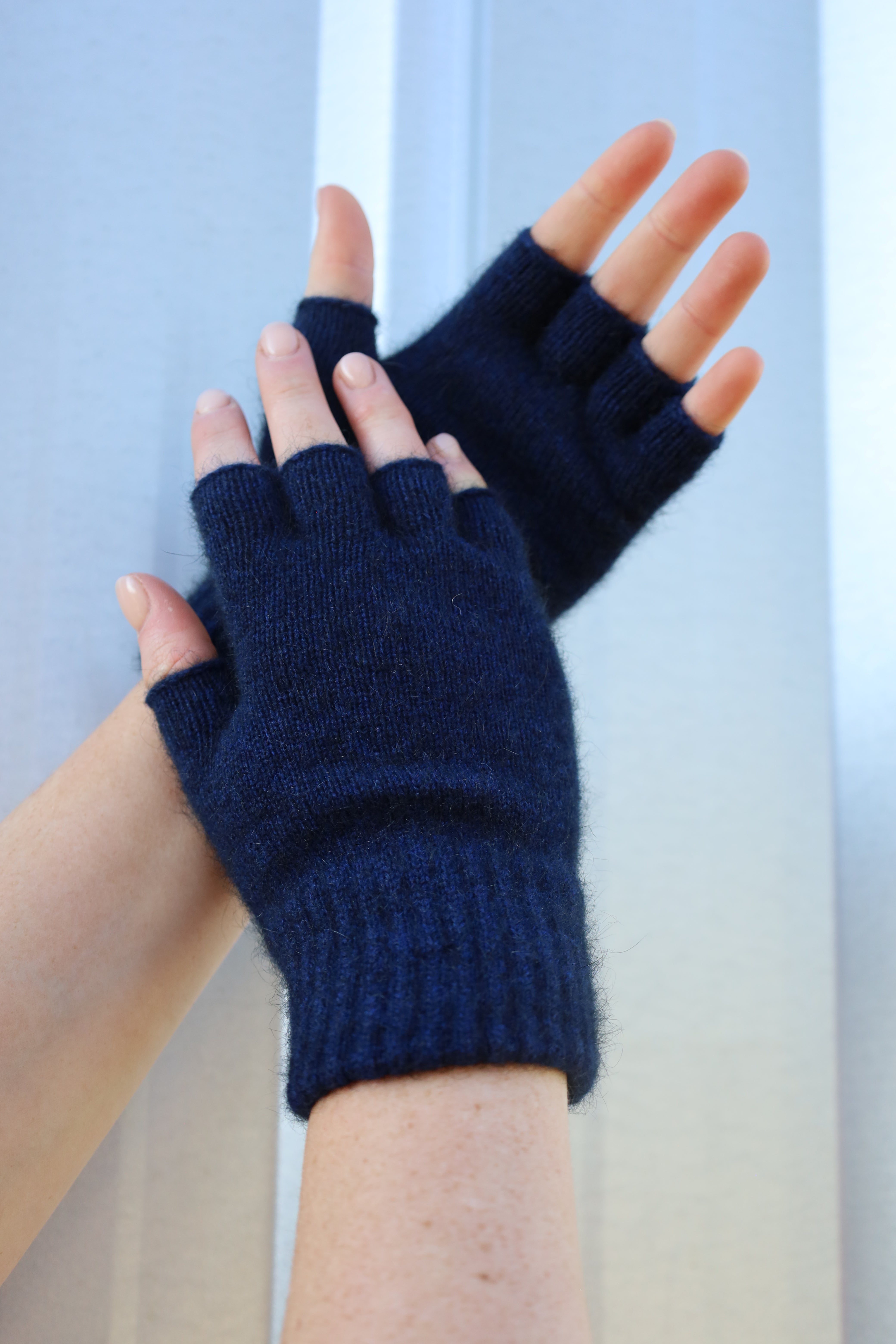 Navy blue fingerless gloves being worn on a light background