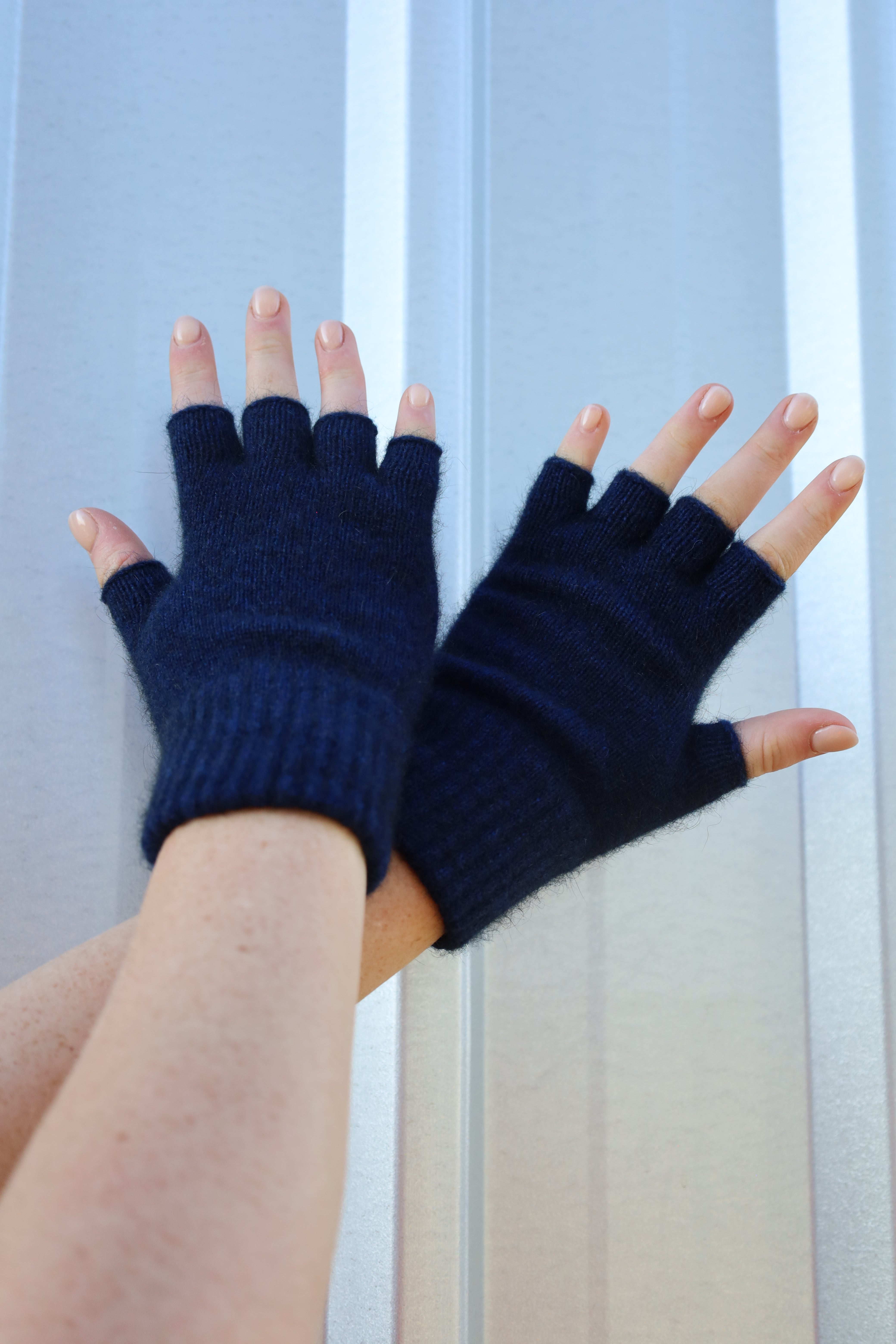 Navy blue fingerless gloves worn on a neutral background