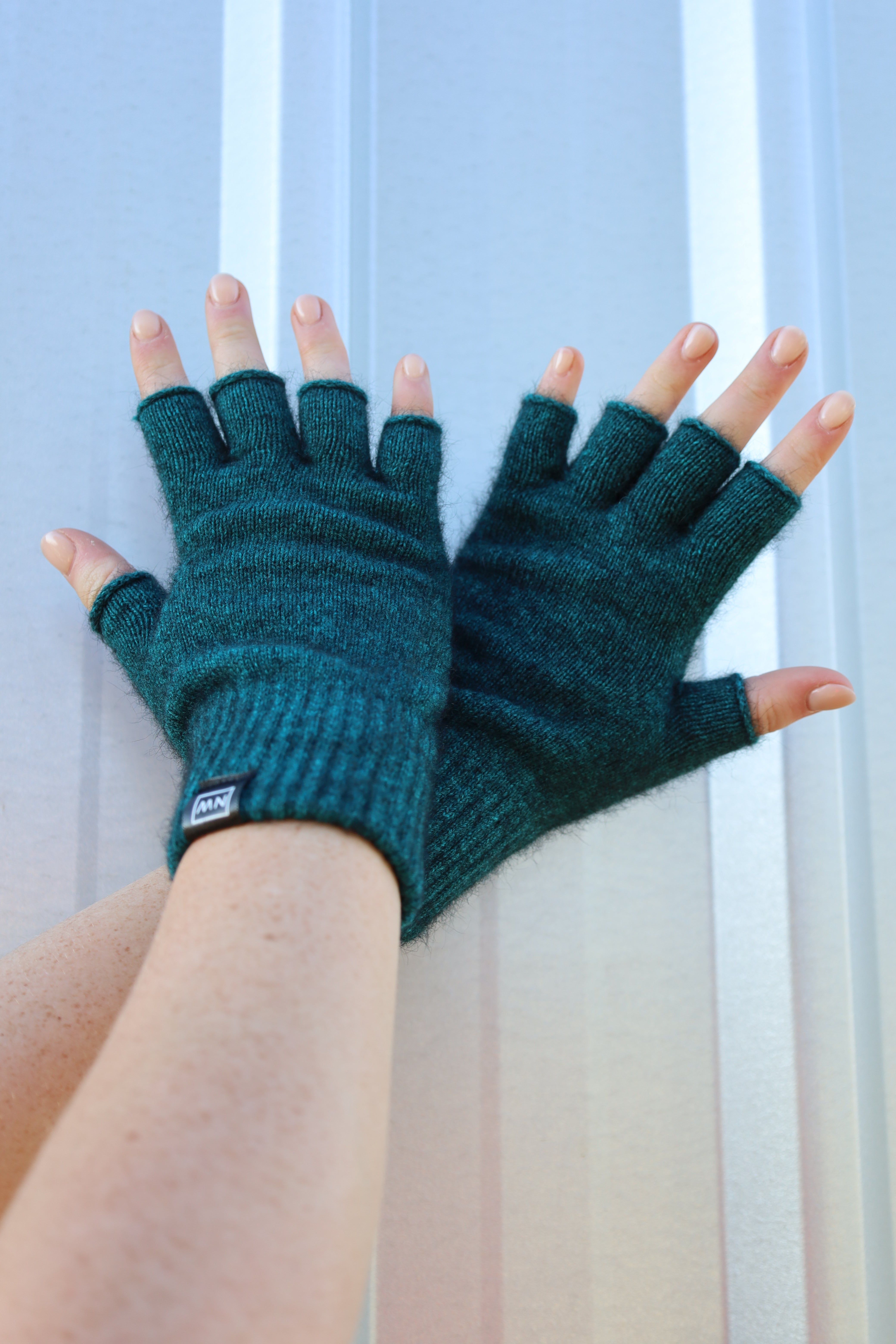 Green fingerless gloves worn by a person on a neutral background