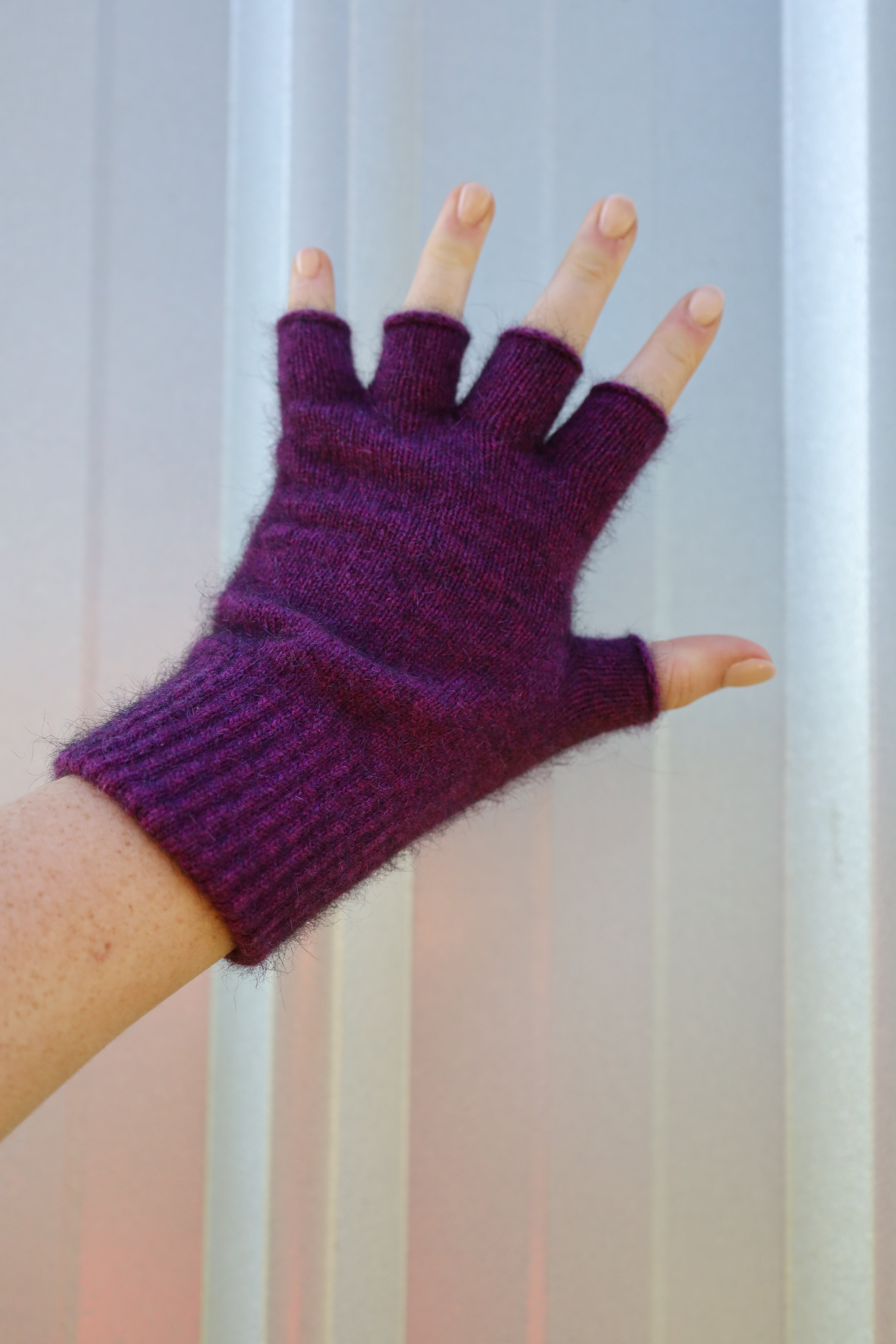Purple fingerless gloves worn on a hand against a neutral background